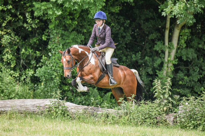 A rider and skewbald horse tackling a cross-country log